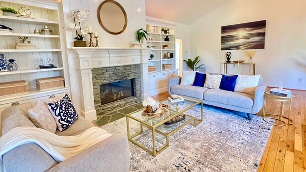 A living room with a fireplace, a sofa, a coffee table, and shelves with decorative items. - New Charming Spacious Disneyland Pool Home (Santa Ana)