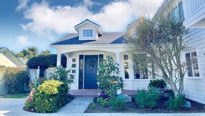 A single-story house with a dark blue front door, a small porch, and a well-maintained garden with various plants and flowers. - New Charming Spacious Disneyland Pool Home (Santa Ana)