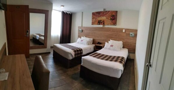 Ett hotellrum med två sängar, ett skrivbord i trä, en spegel och en tavla på väggen.