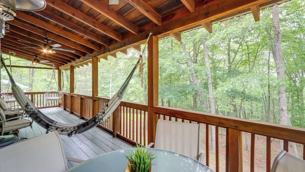Una terraza de madera con una hamaca, sillas y una mesa con una planta en maceta.
