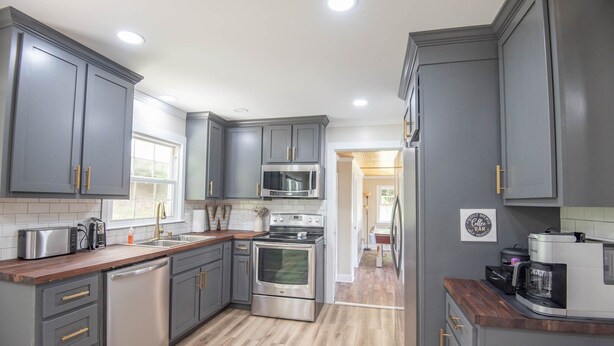A modern kitchen with grey cabinets, stainless steel appliances, and a wooden countertop.