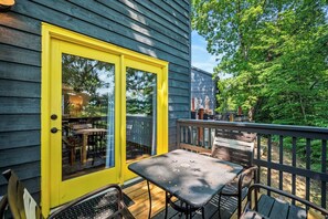 Eine Holzterrasse mit einer gelben Tür, Gartenmöbeln und Blick auf eine von Bäumen gesäumte Gegend.