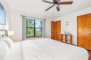 Ein Schlafzimmer mit einem Bett, einem Deckenventilator, einem Fenster mit Vorhängen, einem Kleiderschrank und einem kleinen Regal mit einem Schild.