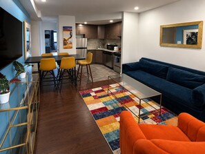 A modern living room with a blue sofa, orange armchair, and a colorful rug.
