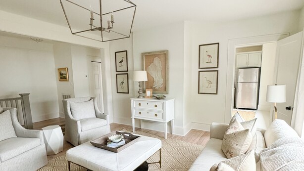 A living room with a geometric chandelier, a white sofa, a patterned rug, and a white cabinet. - The Portico - 2 BR 1 BA Apt (Griffin)