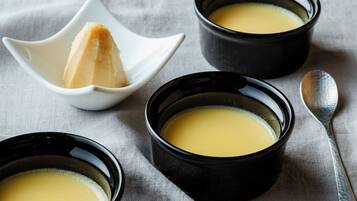 Three black bowls of yellow soup on a textured cloth.