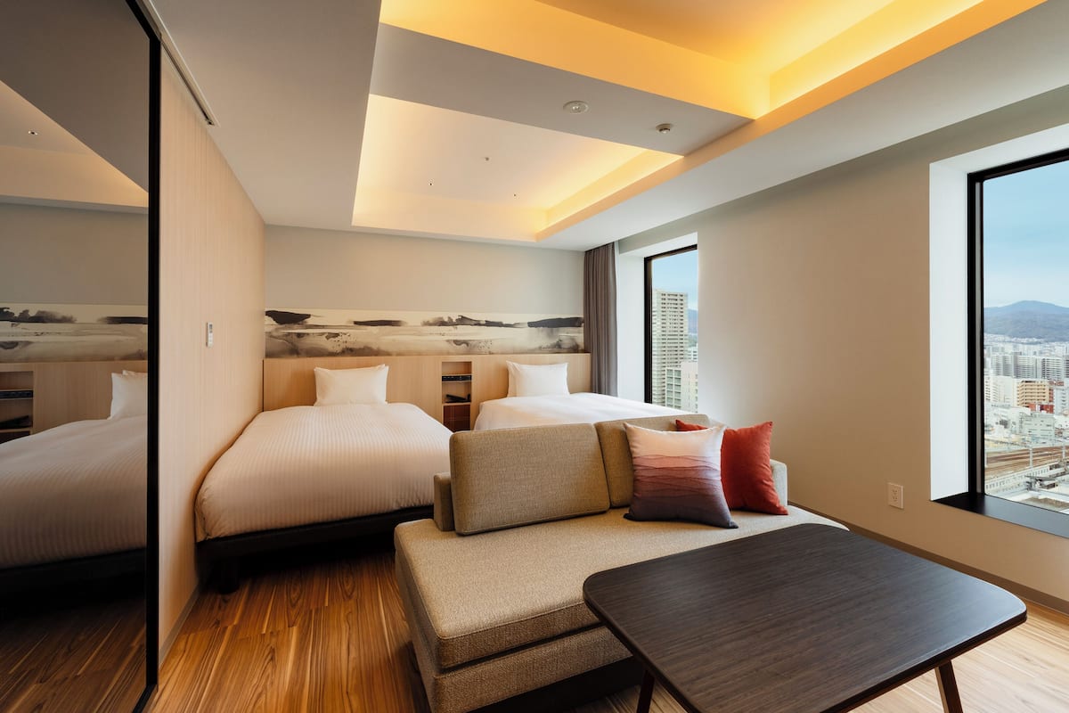 Une chambre d’hôtel moderne avec un grand lit, un canapé, une petite table et une vue sur la ville par une grande fenêtre.