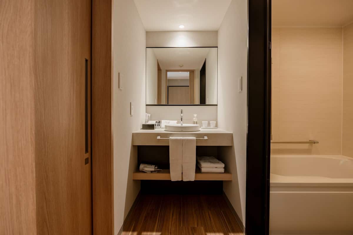 Une salle de bain moderne avec un plancher en bois, un lavabo surmonté d’un miroir et une baignoire.