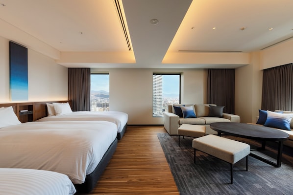 Habitación de hotel con tres camas, un sofá, una mesita de café y vistas a la ciudad.