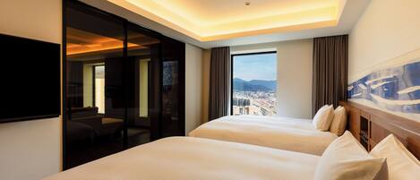 Habitación de hotel con dos camas, un ventanal amplio con vistas a la ciudad y un televisor de pantalla plana montado en la pared.