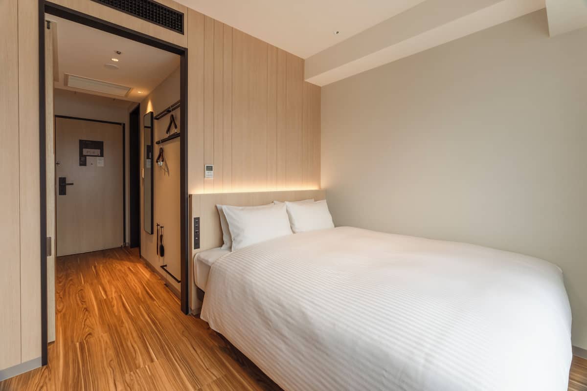 Une chambre d’hôtel avec un plancher en bois, un grand lit avec une literie blanche, une table de chevet et un luminaire fixé au mur.
