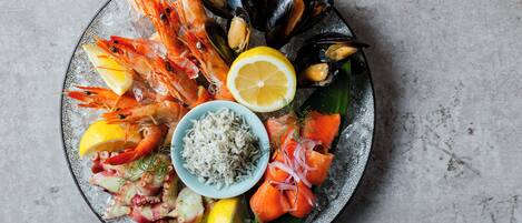 A seafood platter with shrimp, mussels, salmon, and octopus on a plate with lemon slices and a small bowl of rice.