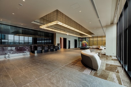 A spacious lobby with a high ceiling, a reception desk, seating area, and large windows.