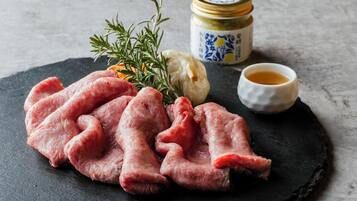 Rohes Fleisch, ein Rosmarinzweig, eine Knolle Knoblauch, ein Glas Sauce und eine kleine Schale Sauce auf einer Schieferplatte.