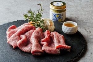 Rohes Fleisch, ein Rosmarinzweig, eine Knolle Knoblauch, ein Glas Sauce und eine kleine Schale Sauce auf einer Schieferplatte.