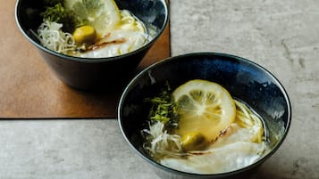 Two bowls of a clear soup with lemon slices and vegetables on a marble surface.