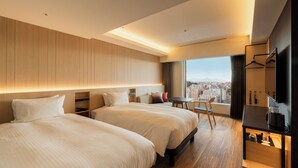 Una habitación de hotel moderna con dos camas, una mesita, un televisor y vistas a la ciudad.