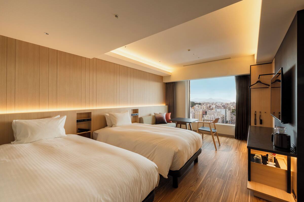 Une chambre d’hôtel moderne avec deux lits, une petite table, une télévision et une vue sur la ville.