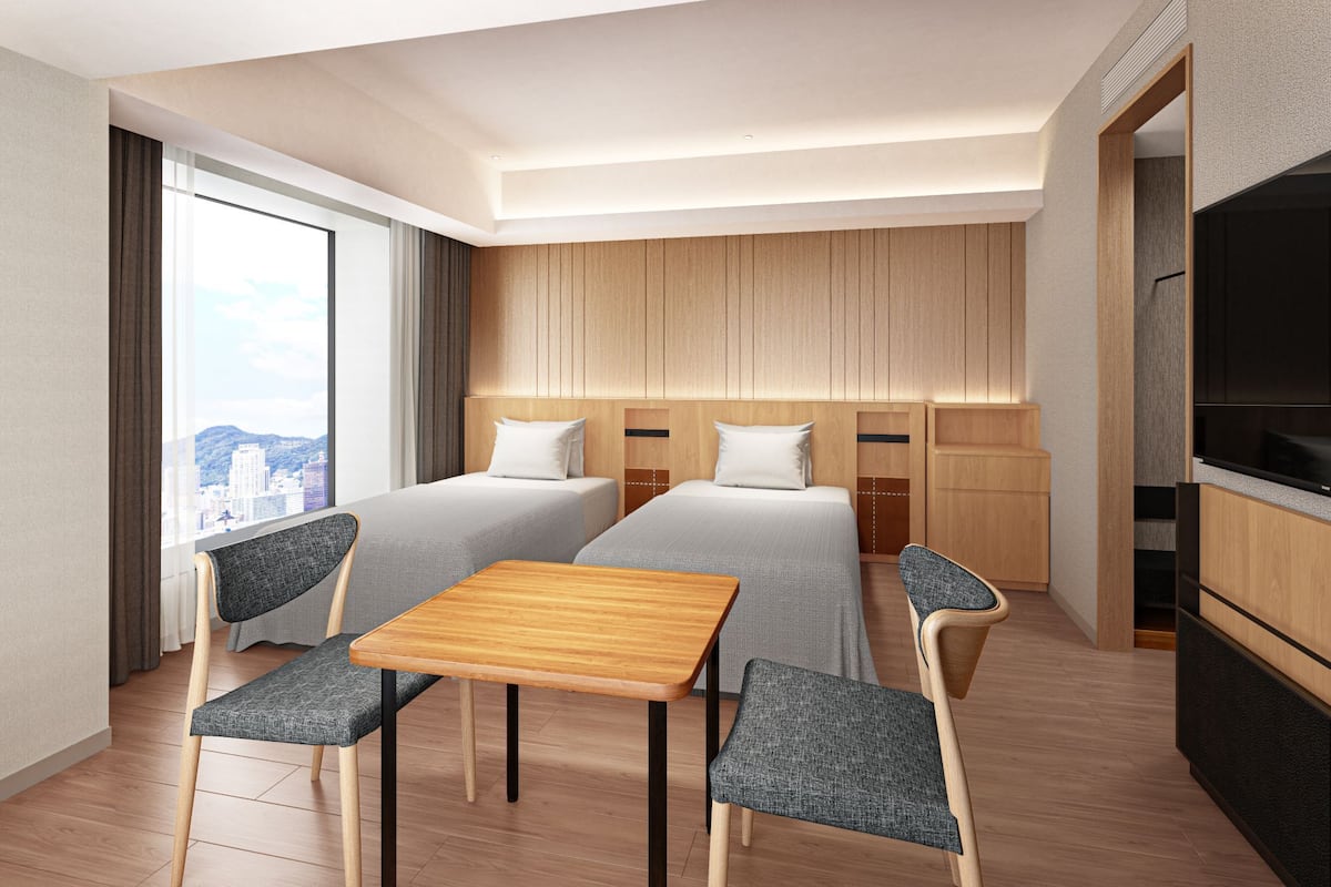 Une chambre d’hôtel avec deux lits, une table en bois, deux chaises, un téléviseur et une vue sur la ville.