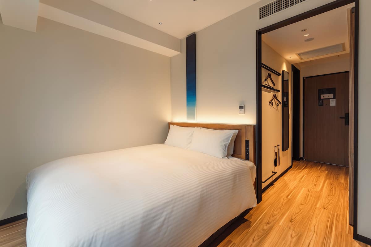 Une chambre d’hôtel avec un grand lit, un plancher en bois, un porte-serviettes fixé au mur et une porte donnant sur un couloir.