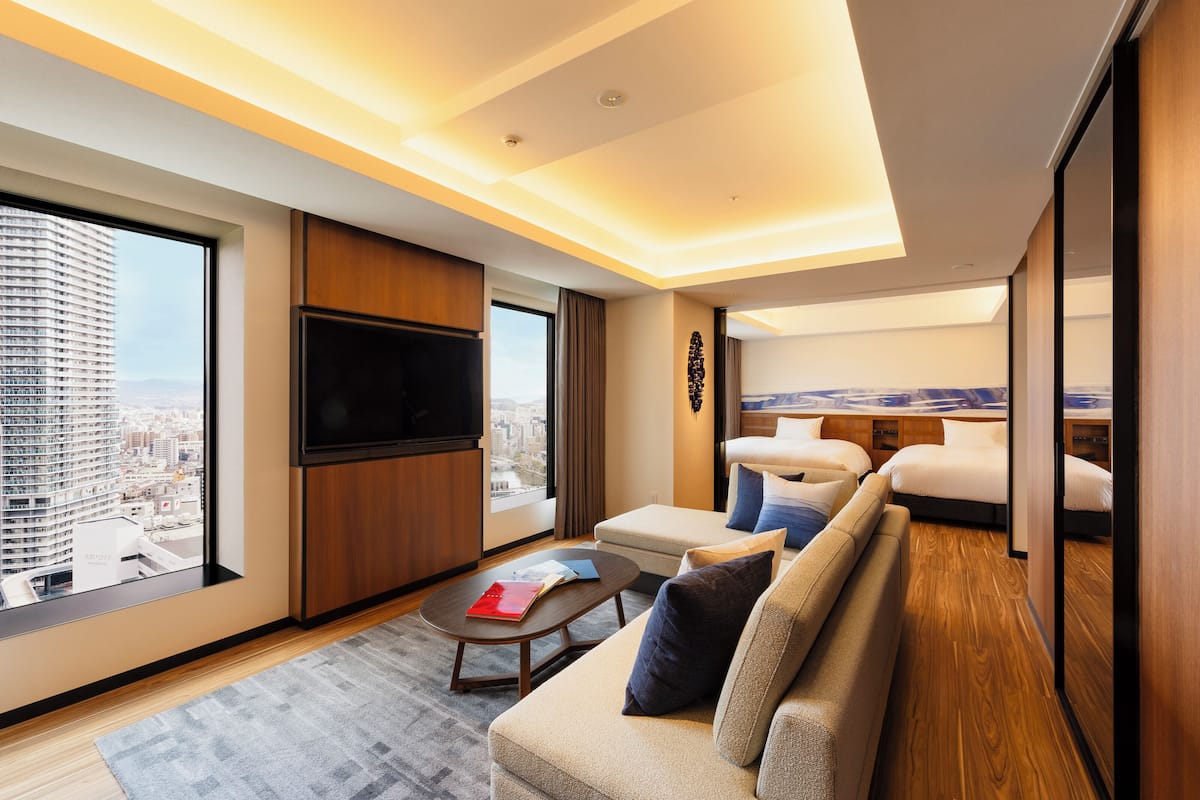 Une chambre d’hôtel moderne dotée d’une grande fenêtre, d’un téléviseur à écran plat, d’un canapé et d’une petite table.