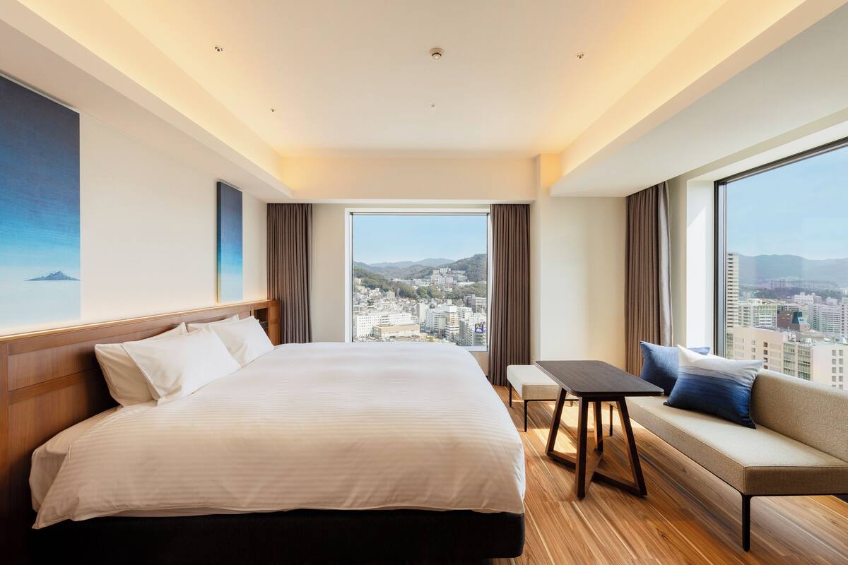 Une chambre d’hôtel avec un grand lit, un canapé, une petite table et une vue sur la ville.