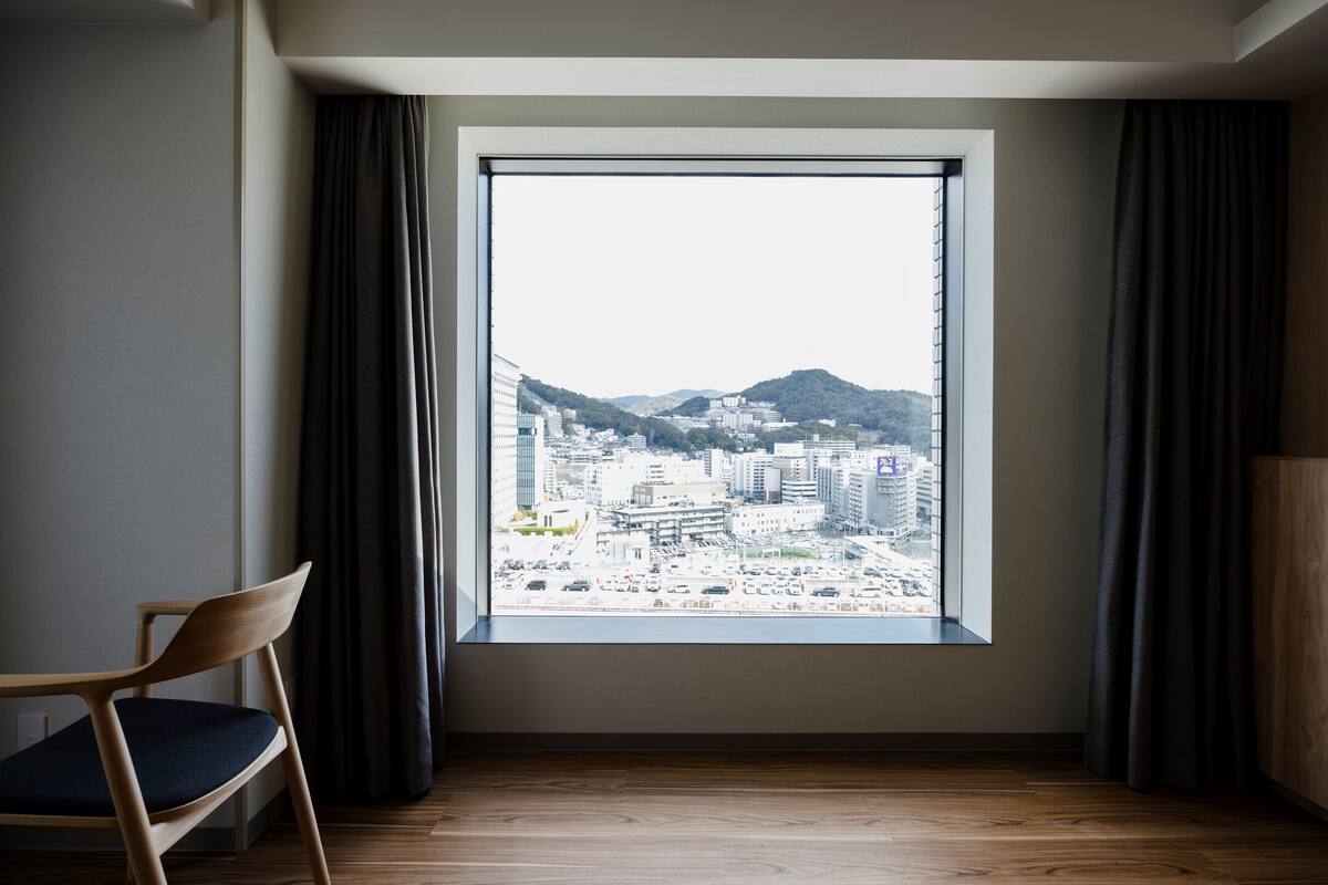 Une pièce dotée d’une grande fenêtre, d’un plancher en bois et d’une chaise avec un coussin.
