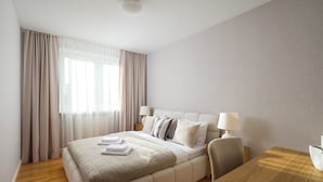 Habitación de hotel con una cama grande, dos mesitas de noche con lámparas, un escritorio de madera y un papel tapiz estampado.