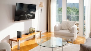 Una sala de estar moderna con una televisión de pantalla plana, una mesa de centro de vidrio, un sofá blanco y un banco de madera.