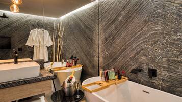 Un bagno moderno con una parete in marmo, una vasca da bagno bianca, un lavandino e un mobile vanitario.