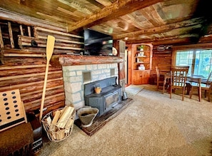 A rustic cabin interior with a stone fireplace, wooden furniture, and a television mounted on the wall.