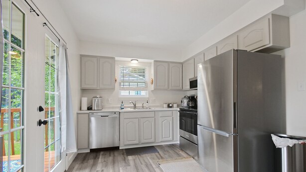 A modern kitchen with white cabinets, stainless steel appliances, and a wooden floor. - Wheels Trails and Tails Inn - Fully Fenced! 2x King 2x Twin Pet Friendly (Boonville)