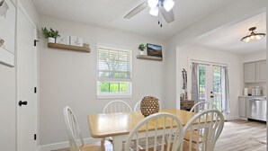 A dining area with a wooden table and white chairs, a ceiling fan, and a view of the outdoors through a window. - Wheels Trails and Tails Inn - Fully Fenced! 2x King 2x Twin Pet Friendly (Boonville)