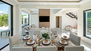 Un'area pranzo moderna con un tavolo in vetro, diverse sedie e un'elegante composizione floreale al centro.