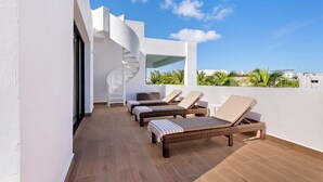 Une terrasse sur le toit avec trois fauteuils de jardin en osier, un escalier en colimaçon et une vue sur les palmiers.