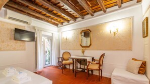A hotel room with a bed, a table with chairs, a TV, a mirror, and a chandelier. - Al Cortile del Moro Suite (Roma)