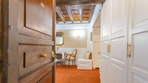 A hallway with a wooden door, a white wall with a mirror, a chair, and a bench. - Al Cortile del Moro Suite (Roma)