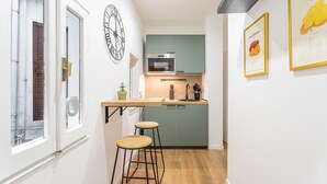 Une cuisine compacte avec un plan de travail en bois, un four encastré et un meuble vert. On y trouve deux tabourets et une plante en pot.