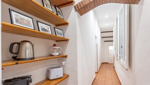 Un couloir étroit, doté d’étagères en bois où sont rangés des appareils de cuisine et des tableaux encadrés.