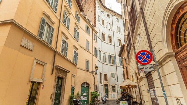 Une rue étroite, bordée de bâtiments des deux côtés, avec un panneau indiquant qu’il est interdit de se garer et une porte verte.