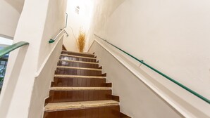 Un escalier avec des marches en bois et une rampe en verre, menant à un palier avec un mur blanc et une petite fenêtre.
