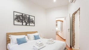 Une chambre d’hôtel avec un lit en bois, du linge de lit blanc, des oreillers bleus et une œuvre d’art encadrée représentant un arbre.