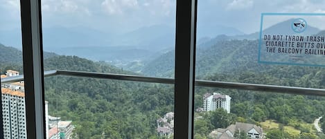 A balcony with a view of a mountainous landscape, a warning sign about not throwing trash, and a glimpse of residential buildings below.