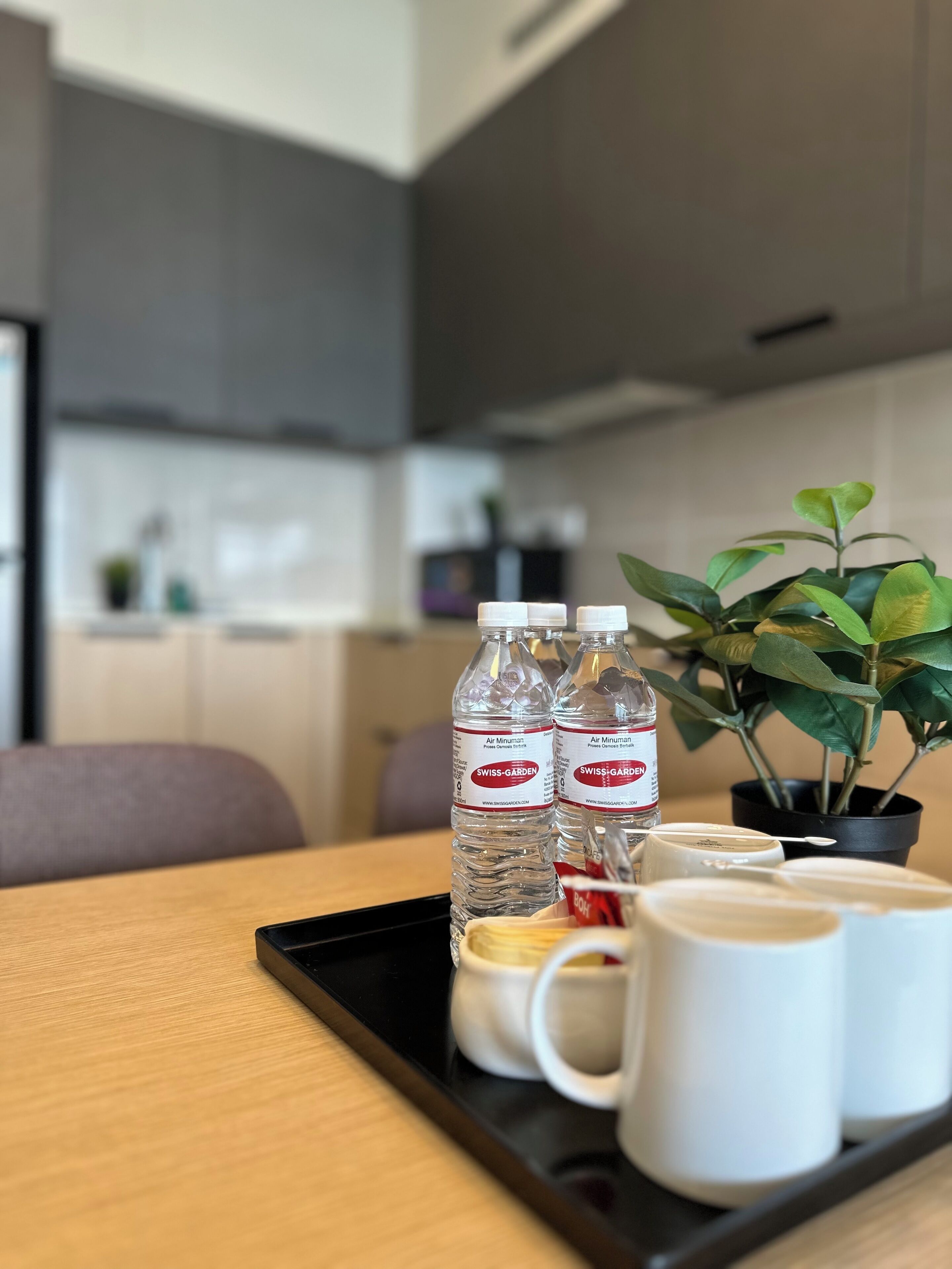 Una bandeja con dos botellas de agua, una taza y un tazón pequeño sobre una mesa de madera en una cocina moderna.