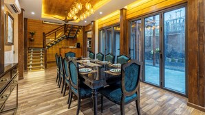 Un espace repas avec une table et des chaises en bois, un escalier et de grandes fenêtres.