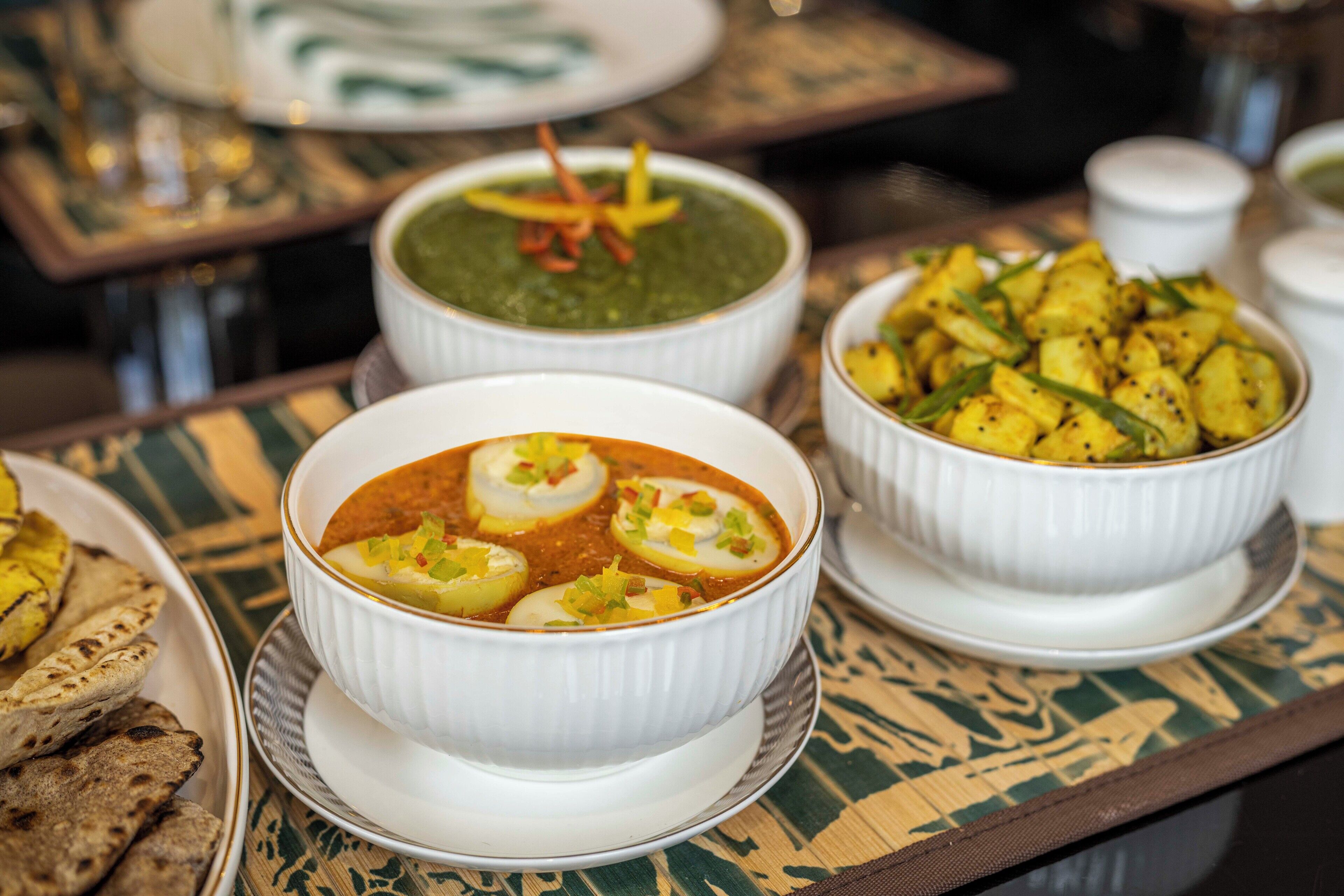A table with various dishes including a bowl of soup with eggs and a bowl of green sauce, and another with roasted potatoes.