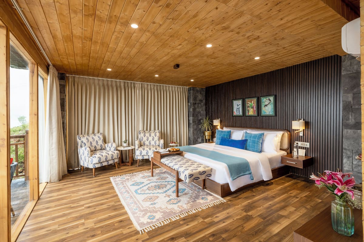 Une chambre avec un plafond en bois, un lit avec une literie bleue, un banc, une chaise, une petite table et un tapis.