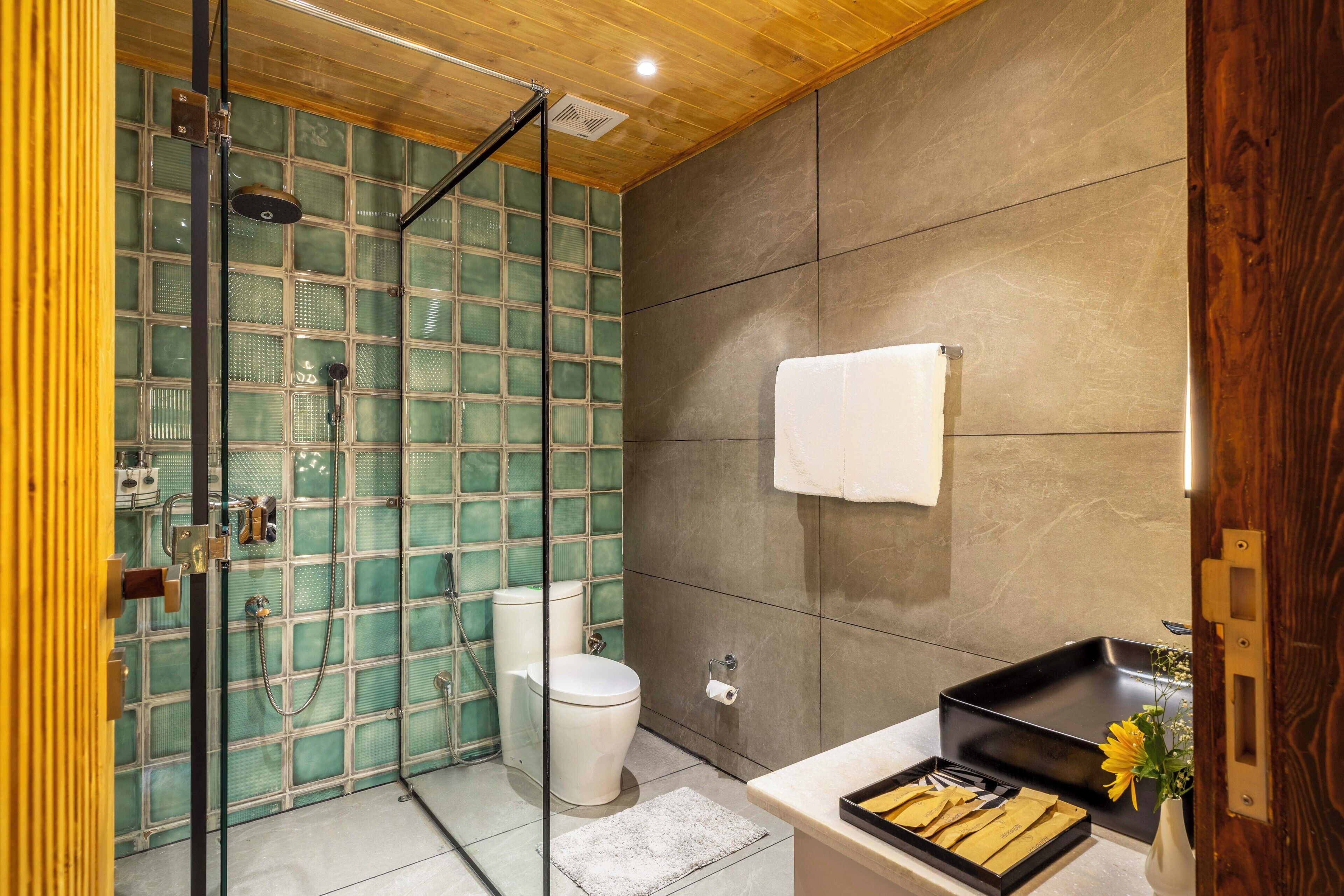 Un baño con cabina de ducha de vidrio, inodoro y lavamanos con una bandeja de toallas.