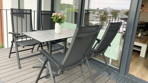 A balcony with a table and chairs, a vase with flowers, and a view of buildings. - Haus Wernerwald - Haus Wernerwald Fewo 6 - Traumhafte Strandnahe Ferienwohnung mit Meerblick (Cuxhaven)
