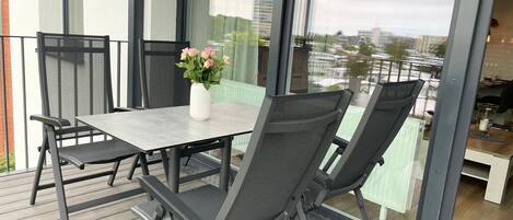Un balcón con una mesa y sillas, un florero con flores y vistas a edificios.